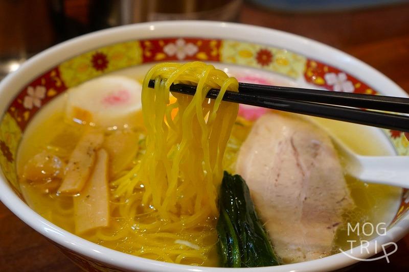 「函館塩ラーメン しなの」の、塩ラーメンの麺を箸で持ち上げている様子